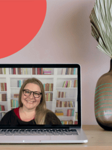 A computer screen shows a picture of Marina in front of a bookshelf. Behind the computer is a pale wall and a bit of a plant is shown to the right.