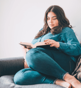 A woman cozied up in the corner of a sofa reading intently
